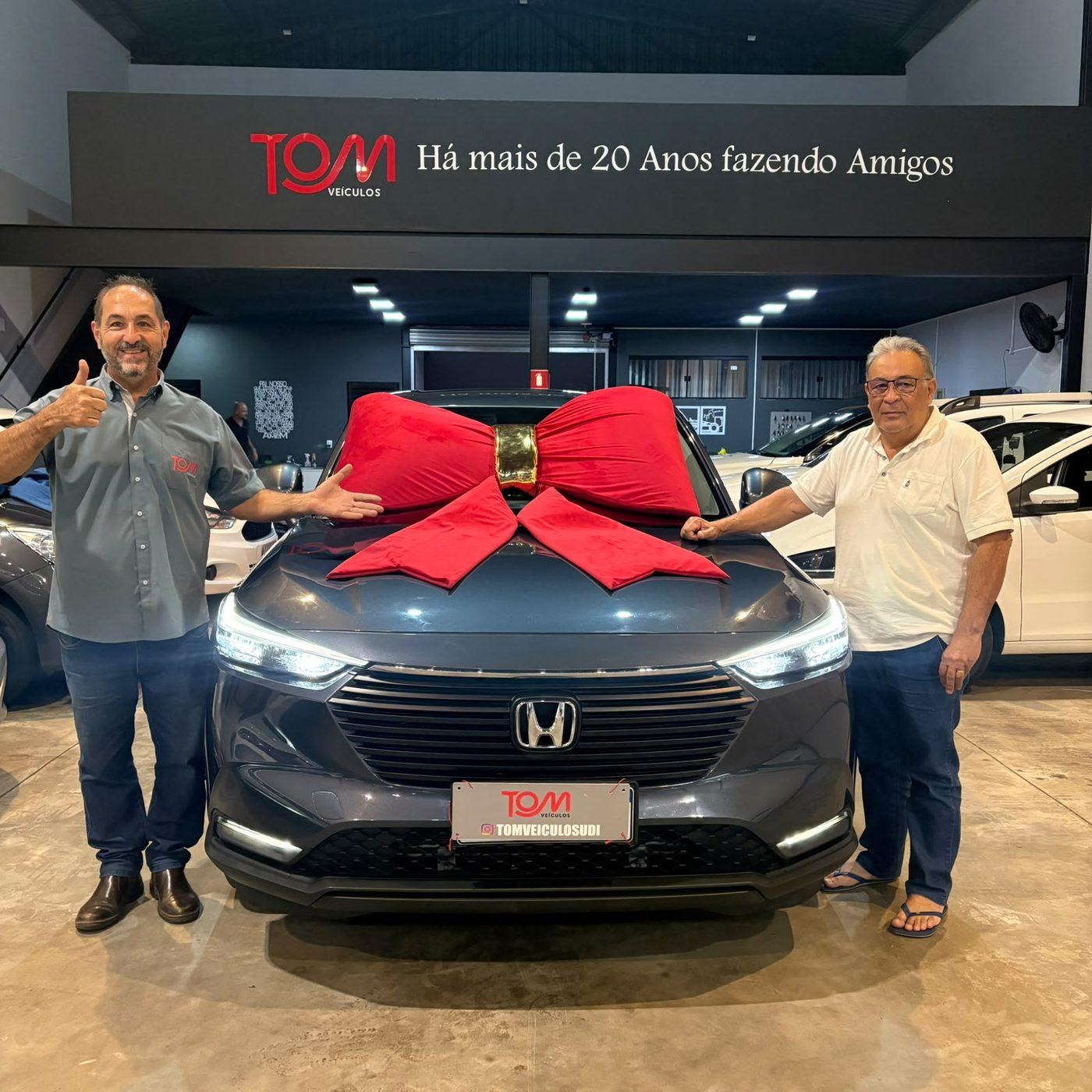 Entrega de veículo na loja da Tom Veículos, cliente ao lado do carro com laço vermelho.